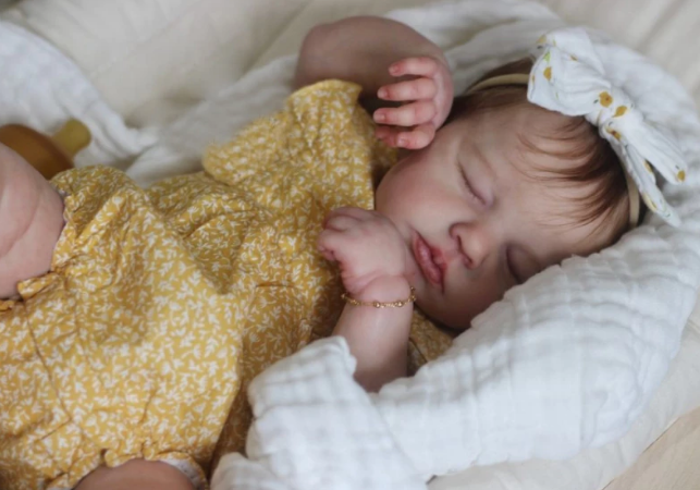 Bebê reborn dormindo com roupa amarela, demonstrando a posabilidade natural do corpo de tecido correto.