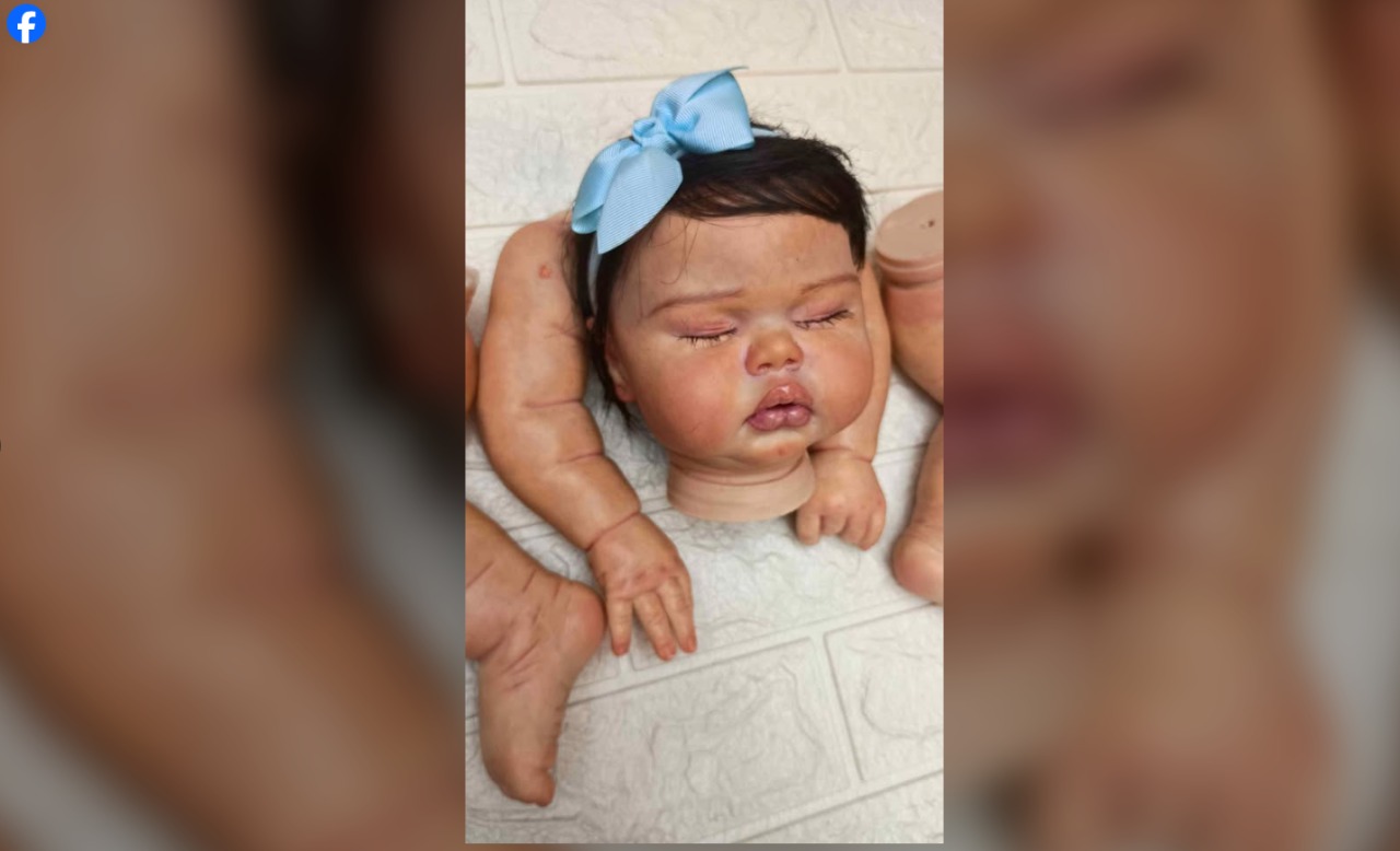 Peças soltas de um bebê reborn (cabeça e membros) já pintados e com laço azul, exemplificando o tipo de material encontrado ao pesquisar kit para montar bebê reborn em grupos de desapego.