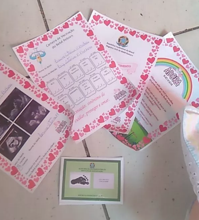 Conjunto de documentos de bebê reborn incluindo certidão de nascimento, teste do pezinho e ultrassom, usados para comprovar a originalidade da arte.