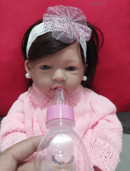 Bebê reborn com feições realistas sendo alimentada com mamadeira, ilustrando o nível de interação buscado em modelos de silicone sólido.